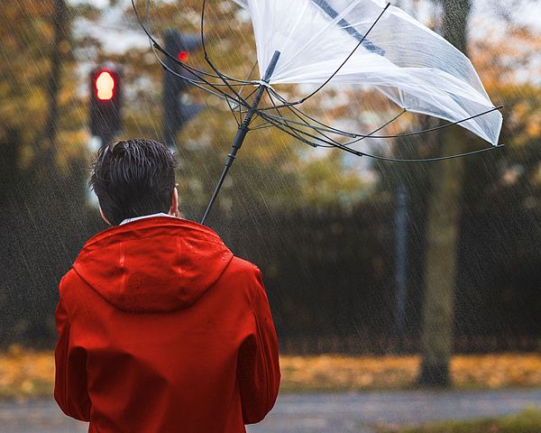 Mann geht mit Regenschirm der durch starken Wind umgebogen wird.