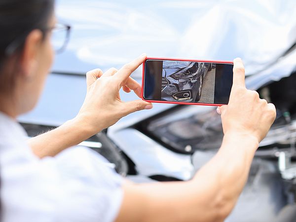 Eine Frau macht mir ihrem Smartphone ein Foto vom entstandenen Schaden an ihrem Auto.