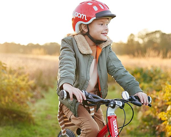 Mädchen mit rotem Helm von woom fährt mit ihrem woom Fahrrad einen Feldweg entlang.