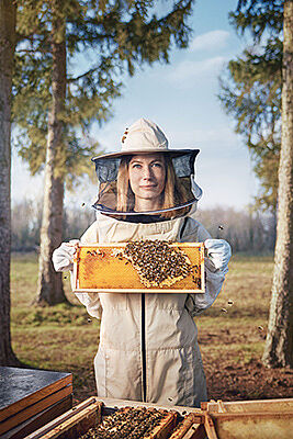 Eine Imkerin steht im Wald bei ihren Bienenvölkern und zeigt Honigwaben in die Kamera 