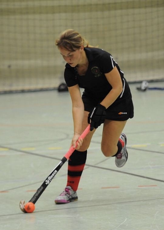Eine Frau in Sportbekleidung spielt Floor Hockey. Sie hält dabei einen Schläger in der Hand und schießt einen Ball