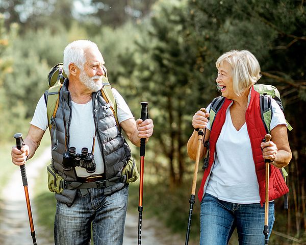 Ein glückliches Seniorenpaar wandert mit Nordic-Walking-Stöcken durch den Wald.