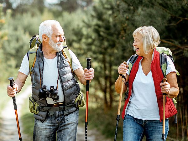 Ein glückliches Seniorenpaar wandert mit Nordic-Walking-Stöcken durch den Wald.