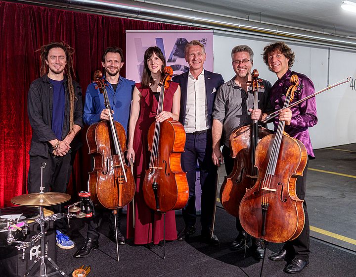 Auf dem Bild sieht man 5 Musiker:innen mit Chellos und Schlagzeug