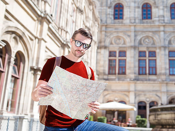 Ein Tourist steht mit dem Stadtplan von Wien vor der Wiener Staatsoper.