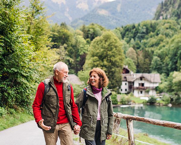 Ein glückliches Seniorenpaar in Wanderklamotten spaziert entlang eines Sees.