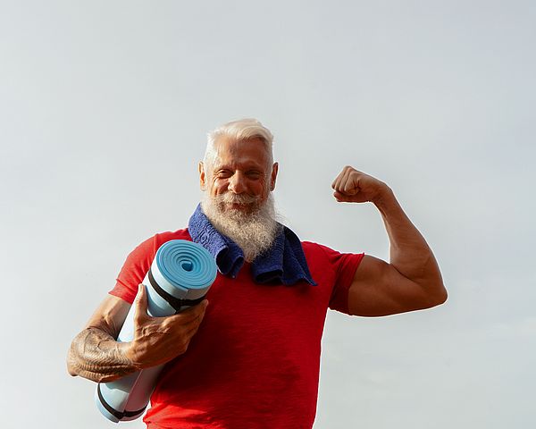 Ein muskulöser Senior posiert im Freien mit einer Gymnastikmatte in der Hand.