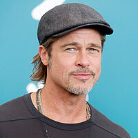 Bild von Schauspieler Brat Pitt im schwarzen Oberteil mit grauer Mütze vor einer türkisfarbenen Wand.
