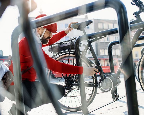 Ein Mann in Sportbekleidung sperrt sein Fahrrad bei einem Fahrradständer ab.