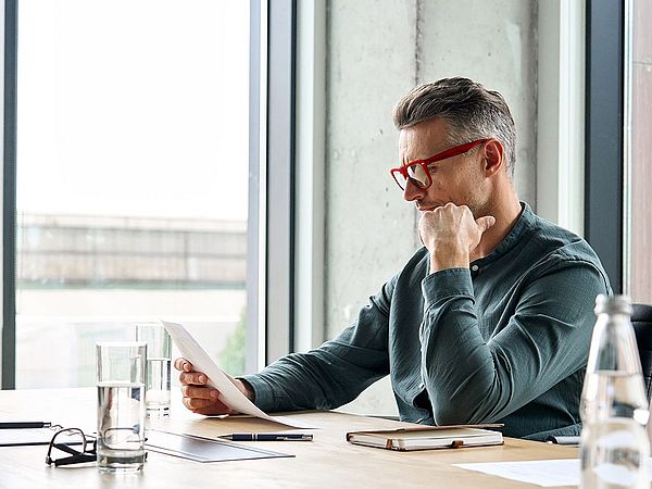 Ein Mann mit Brille liest konzentriert am Schreibtisch.
