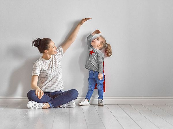 Mutter zeigt ihrer kleinen Tochter mit der Hand wie groß sie schon ist.