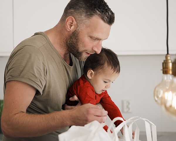 Ein Vater hält sein Kind im Arm. Dabei schauen beide voller Neugier in eine Tasche