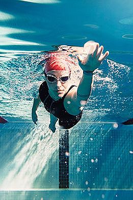 Eine Schwimmerin befindet sich im Becken unter Wasser und schwimmt ihre Bahnen. Dabei hat sie eine Schwimmhaube und eine Taucherbrille auf.