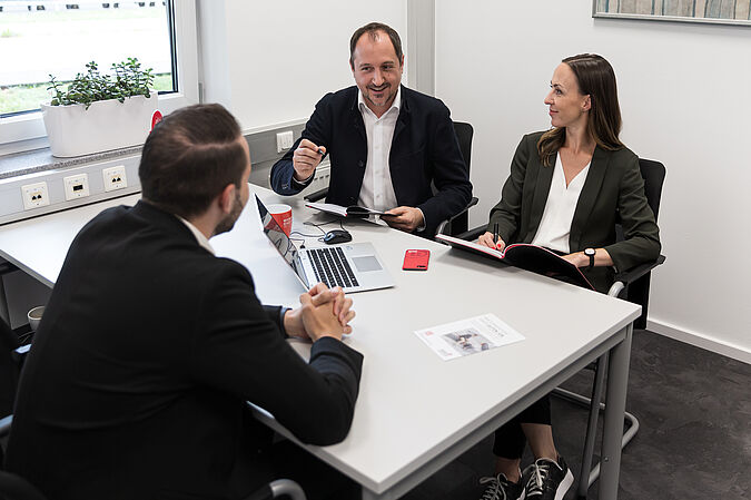 Drei Personen sitzen in einem Büro beisammen und unterhalten sich.