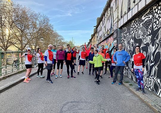 Gruppe von Mitarbeiterinnen und Mitarbeitern der Wiener Städtischen, welche sich zum gemeinsamen Laufen verabredet haben. Sie befinden sich dabei mitten in der Stadt auf einer Straße.