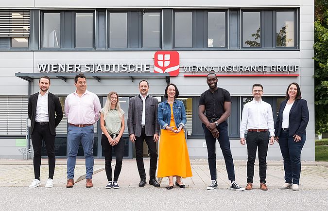 Mehrere Personen stehen vor einem Gebäude und blicken in die Kamera.