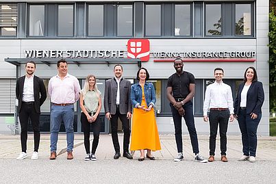 Mehrere Personen stehen vor einem Gebäude und blicken in die Kamera.