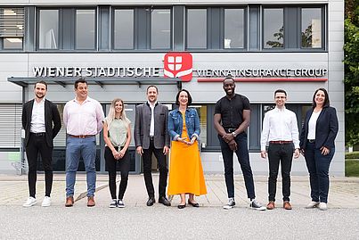 Mehrere Personen stehen vor einem Gebäude und blicken in die Kamera.