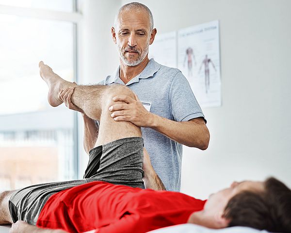 Ein Physiotherapeut behandelt einen Patienten am Bein in seiner Praxis. 