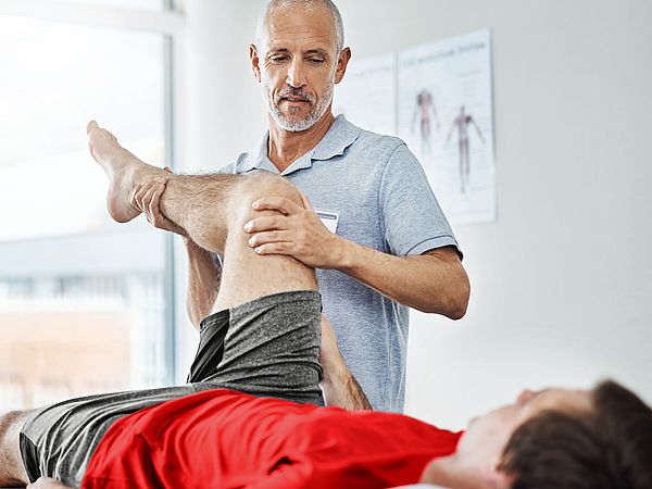 Ein Physiotherapeut behandelt einen Patienten am Bein in seiner Praxis. 