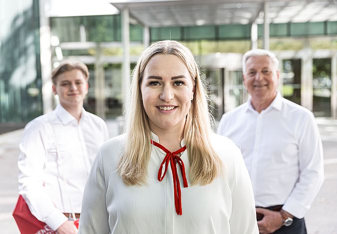 Drei Personen mit weißen Hemden lächeln in die Kamera.