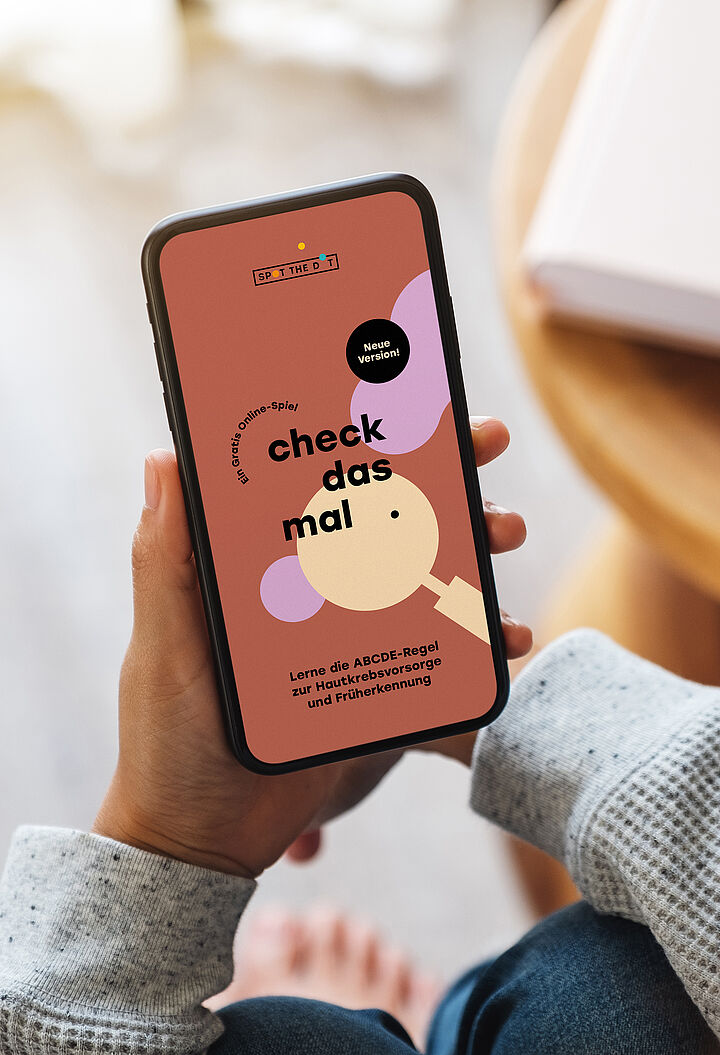 Eine Person hält ein Smartphone, auf dessen Bildschirm die Website „check das mal“ angezeigt wird.