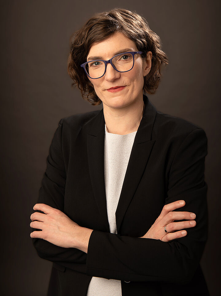 Porträtfoto von einer Frau mit kinnlangen braunen Haaren in schwarzem Sakko und mit verschränkten Armen