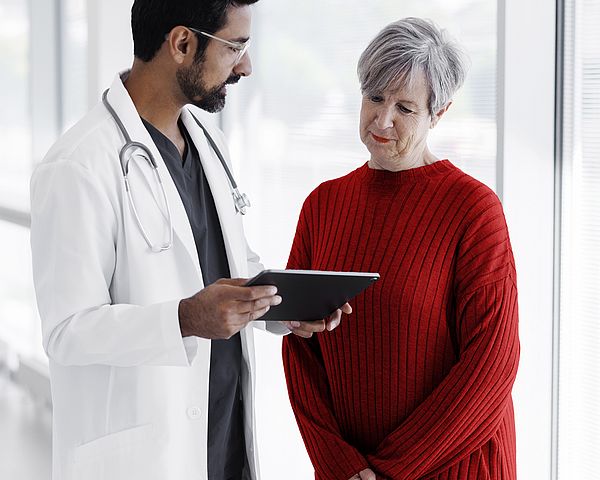 Eine ältere Dame spricht mit einem Arzt während beide auf ein Tablet schauen