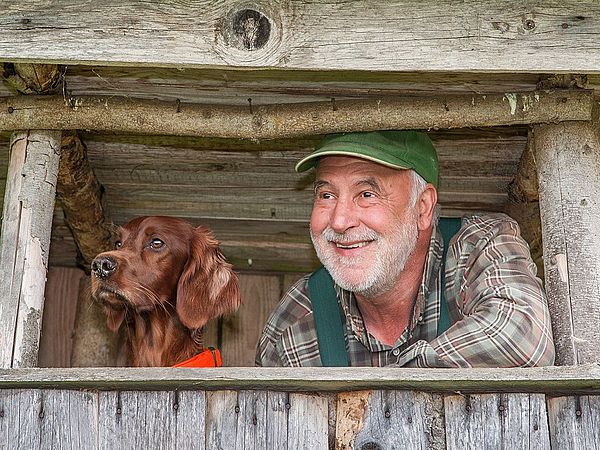 Ein Jäger ist mit seinem Hund am Hochstand im Wald und blickt in die Ferne.