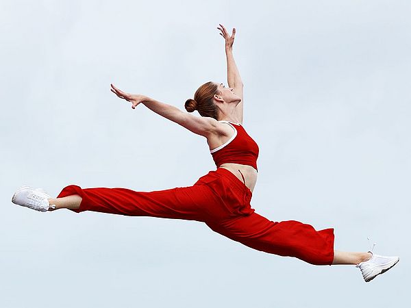 Junge blonde Frau in rotem Sportoutfit macht einen hohen Spagatsprung.