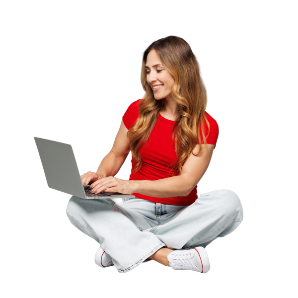 Eine Frau sitzt im Schneidersitz auf einem dunklen Hintergrund. Sie trägt ein rotes T-Shirt, helle Jeans und weiße Sneaker. Auf ihrem Schoß liegt ein silberner Laptop, auf dem sie tippt und dabei lächelt. Ihr langes, leicht gewelltes Haar fällt über die Schultern. Die Szene wirkt freundlich und entspannt.