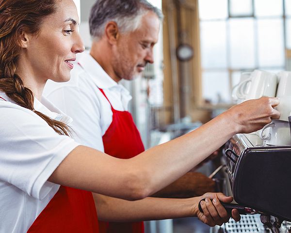 Ein Kellner und eine Kellnerin bedienen eine Kaffeemaschine in einem Restaurant.