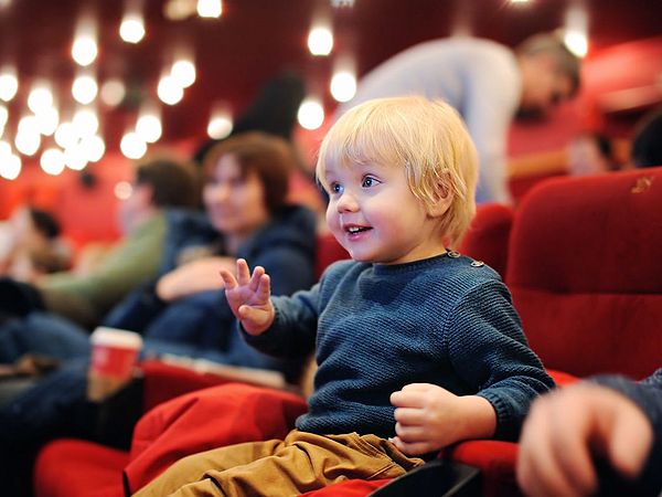 Ein Bub sitzt voller Vorfreude im Kinosaal und schaut gespannt auf die Leinwand