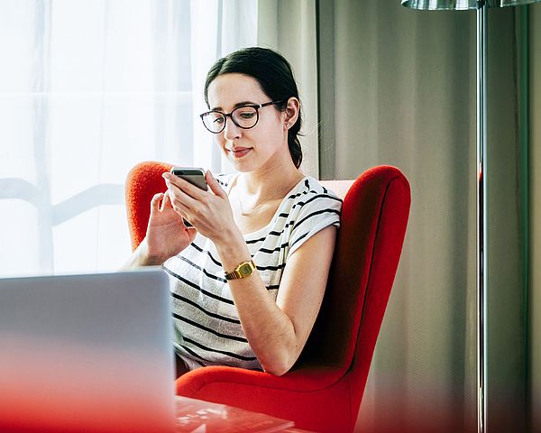 Eine junge Frau sitzt auf einem Stuhl und tippt auf ihr Smartphone.