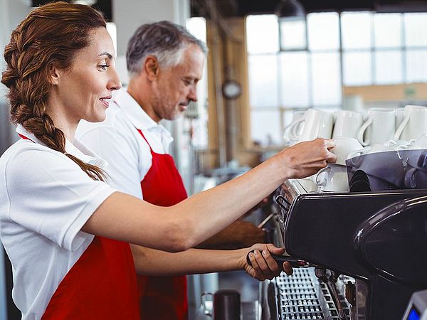 Ein Kellner und eine Kellnerin bedienen eine Kaffeemaschine in einem Restaurant.