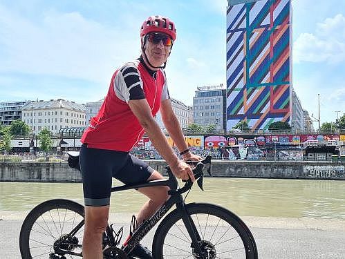 Ein Radfahrer im Trikot der Wiener Städtischen fährt auf seinem Bike eine Strecke entlang. Im Hintergrund ist der Ringturm zusehen. 