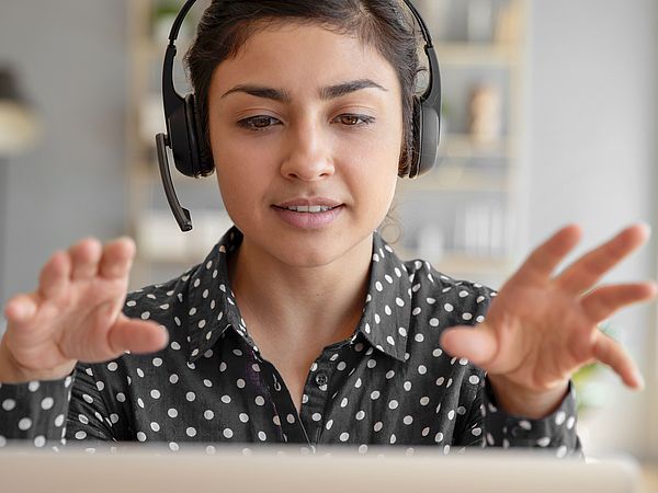 Eine Frau sitzt mit einem Headset vor einem Laptop und führt ein virtuelles Gespräch.