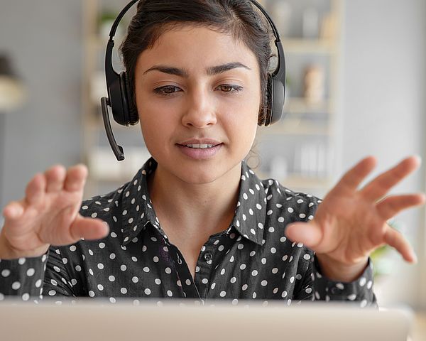 Eine Frau sitzt mit einem Headset vor einem Laptop und führt ein virtuelles Gespräch.