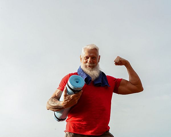 •	Ein muskulöser Senior posiert im Freien mit einer Gymnastikmatte in der Hand.