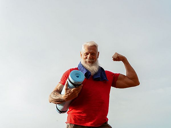 •	Ein muskulöser Senior posiert im Freien mit einer Gymnastikmatte in der Hand.