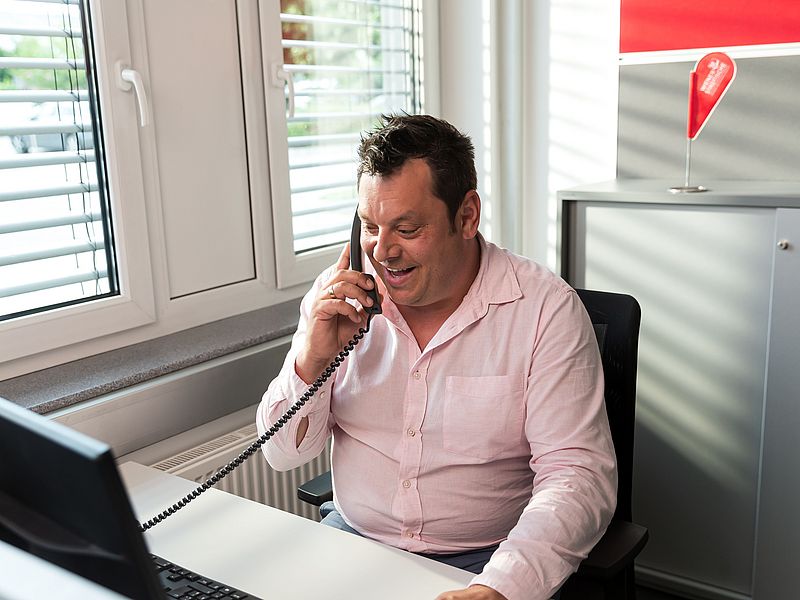 Dunkelhaariger Mann sitzt an seinem Schreibtisch und telefoniert.
