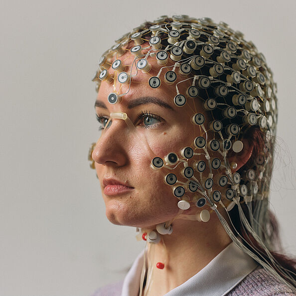 Eine Frau mit strengem Gesichtsausdruck und einem Kinngrübchen, das an Kirk Douglas erinnert, trägt eine Elektrodenkappe und schaut von rechts nach links aus dem Bild heraus. Man sieht nur ihren Kopf.