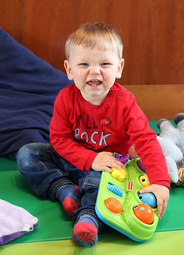 Blonder Junge mit rotem Pullover lächelt in die Kamera.