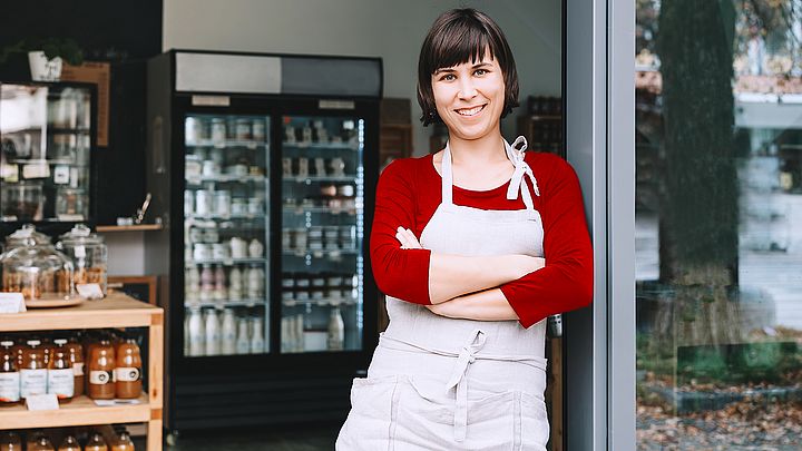 Eine junge Gründerin eines Kaffeehauses steht vor ihrem Geschäft und lächelt dabei voller Freude