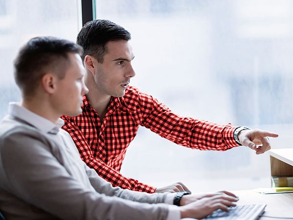 Zwei Geschäftsmänner sitzen in einem Büro und arbeiten gemeinsam fokussiert am Computer.