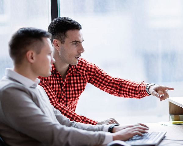 Zwei Geschäftsmänner sitzen in einem Büro und arbeiten gemeinsam fokussiert am Computer.