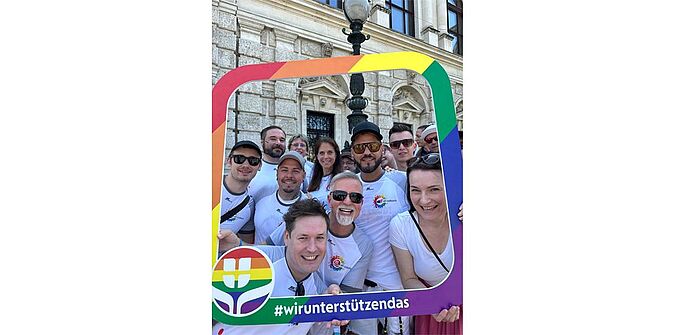 Bild vom All Colours Netzwerk. Leute schaue durch einen Rahmen der ausieht wie ein Regenbogen.