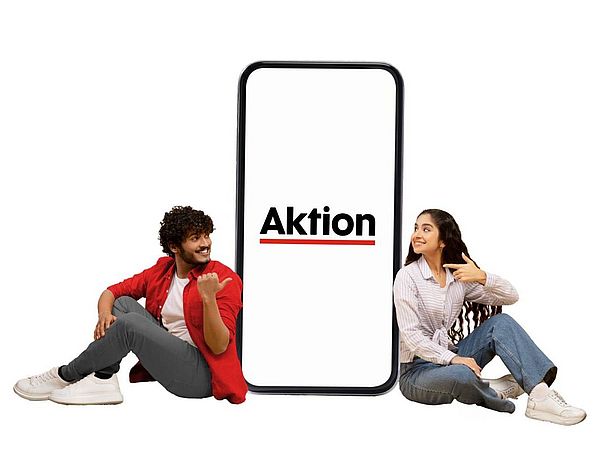 Junger Mann mit dunklen Haaren und junge Frau mit dunklen Haaren sitzen neben einem riesigen Smartphone mit der Aufschrift Aktion.