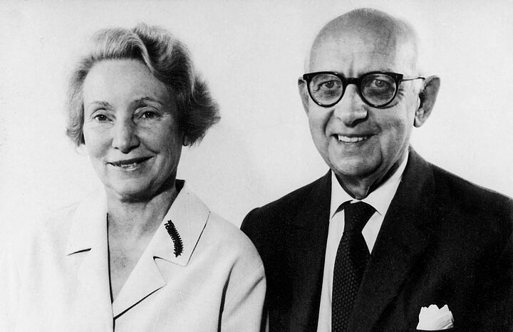 Schwarz-weiß Foto von einem Paar: Sie hat kurze Haare und ein weißes Oberteil, er hat Glatze und Brille und ist im schwarzen Anzug mit Krawatte.
