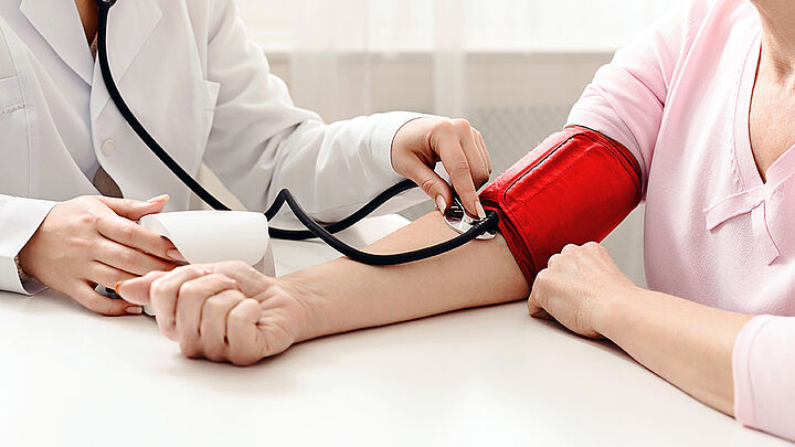 Medizinische Fachangestellte misst den Blutdruck einer sitzenden Person mit einer Blutdruckmanschette am Oberarm.